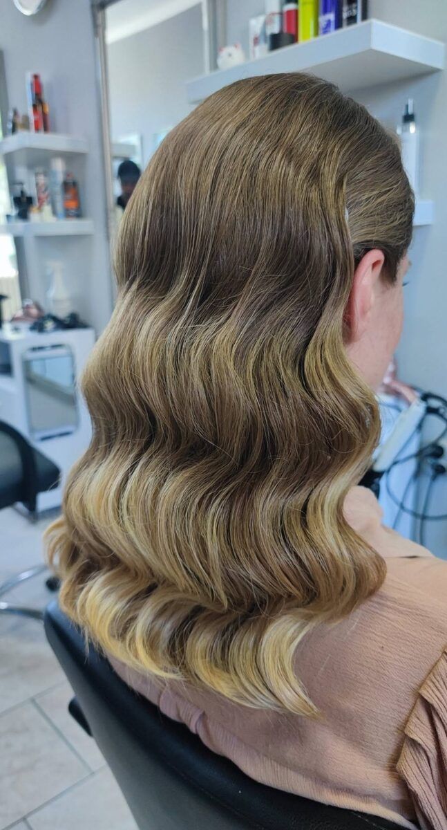 Długie, miodowo-blond włosy ułożone w klasyczne fale w stylu retro, z jaśniejszymi końcówkami.